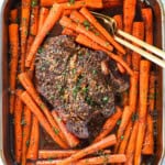 holding the roast in a pan surrounded by carrots that's just come out of the oven
