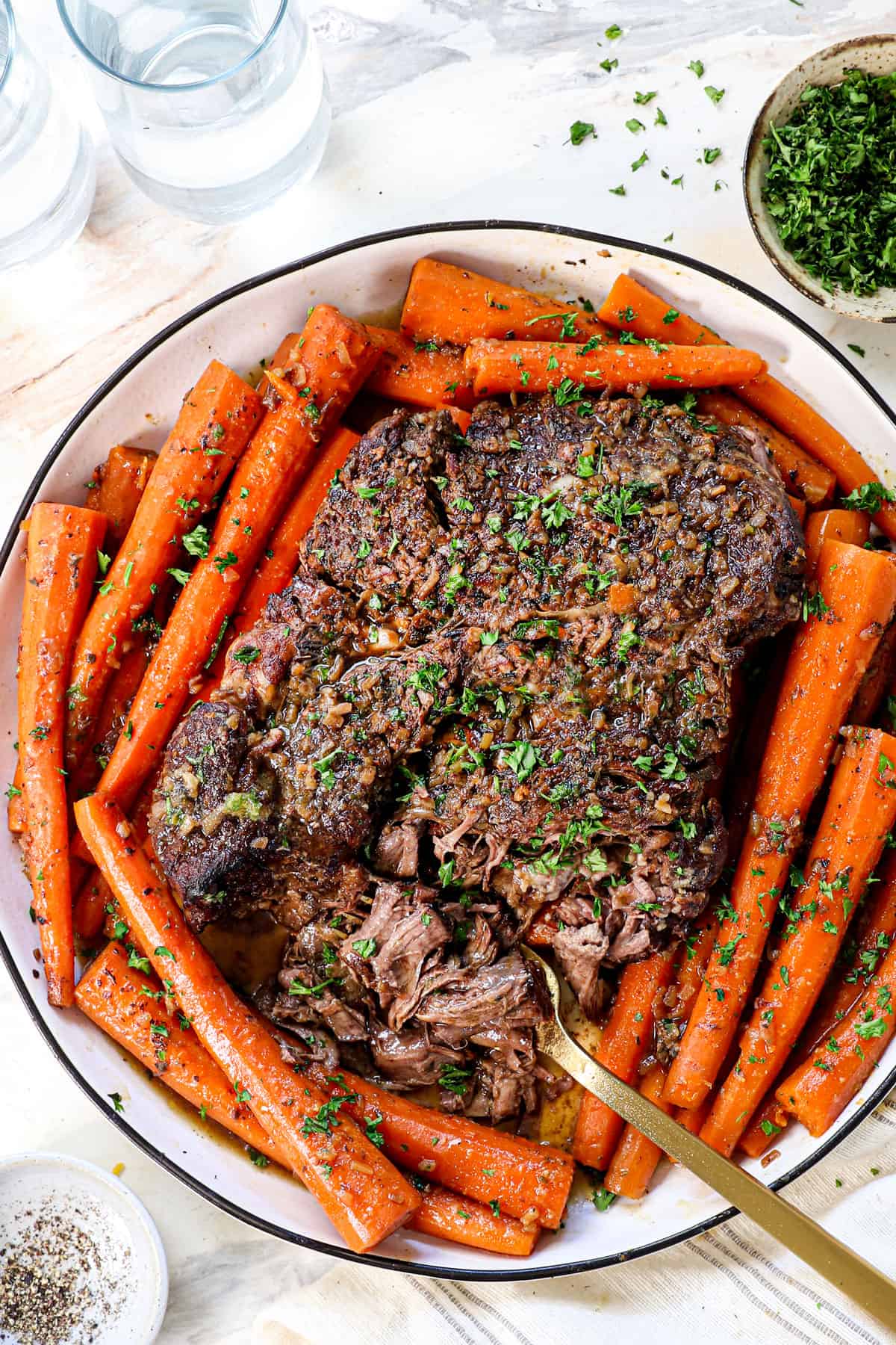top view of serving roast recipe on a platter surrounded by carrots and garnished with parsley