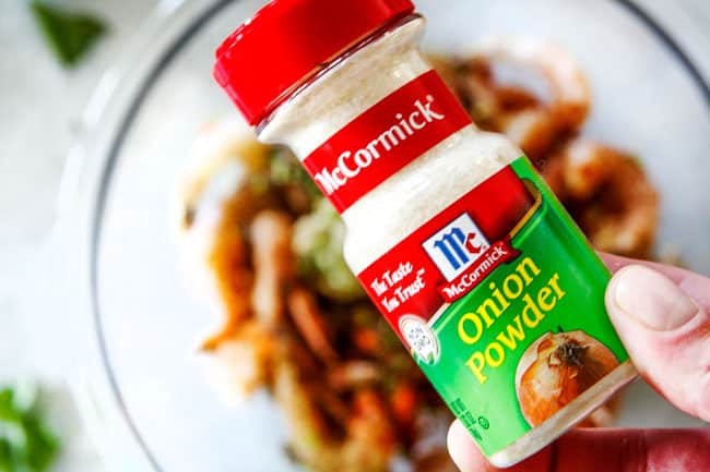 Cilantro Lime Shrimp Tacos EXPLODING with tangy, punchy flavor complimented by sweet refreshing Mango Salsa and silky Avocado Crema on your table in 35 minutes! You can prep the toppings ahead of time for a super quick and easy weeknight dinner that tastes better than any restaurant! showing how to make shrimp tacos by adding raw shrimp to a bowl with onion powder, garlic, paprika, ground cumin, for healthy Shrimp Tacos