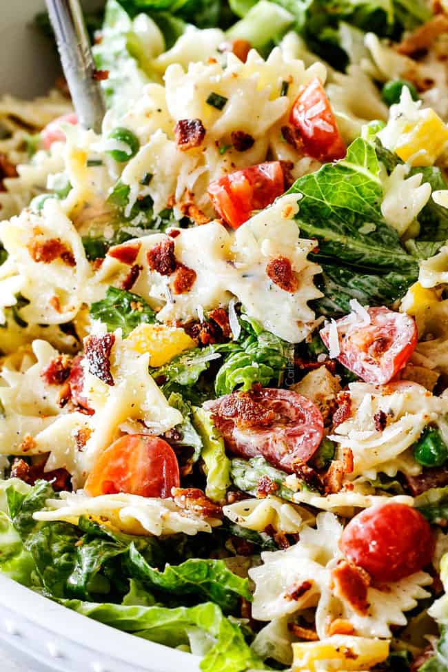 Up close side shot of easy BLT Pasta Salad recipe in a white bowl with tongs lifting salad up