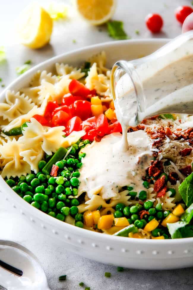 Pouring creamy Lemon Chive Dressing over easy BLT Pasta Salad in a white bowl