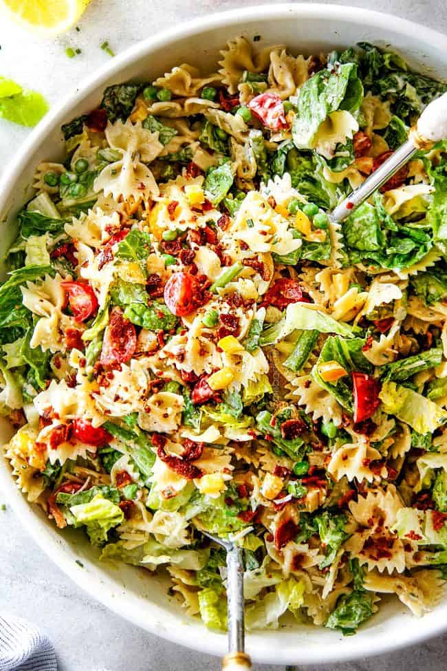 Top Shot of Best BLT Pasta Salad in a white bowl with white tongs lifting the salad up