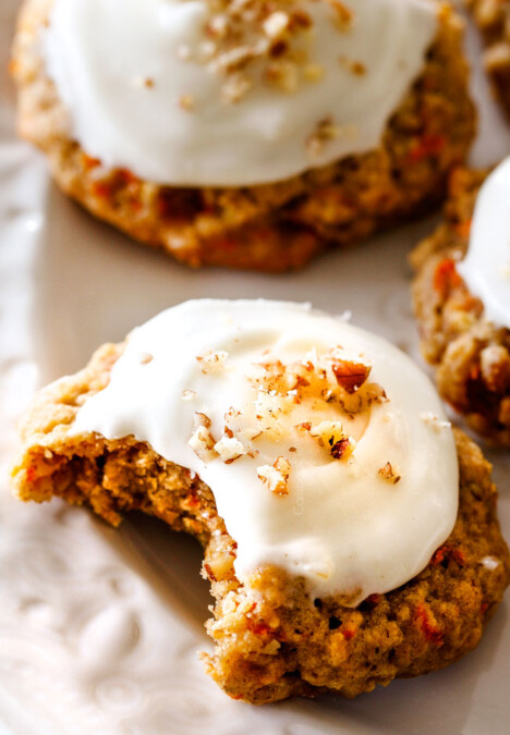 Up close of soft Carrot Cake Cookies with Cream Cheese Frosting with a bite taken out of it on a white plate