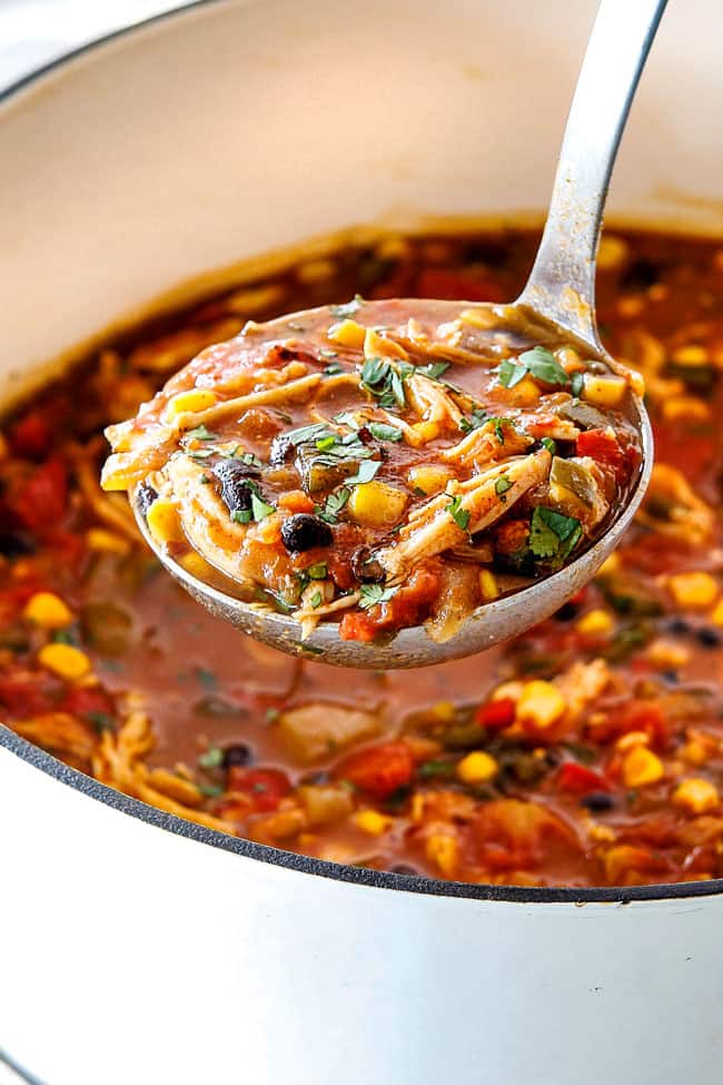 Easy 30-Minute Homemade Chicken Tortilla Soup that tastes better than any restaurant! It's accidentally healthy, easy to double/triple for a crowd, freezer friendly and tastes like it's been simmering for hours but on your table in 30 Minutes! Up close of ladeful of easy Chicken Tortilla Soup in a white dutch oven with a spoonful of soup loaded with chicken, beans, corn, and tomatoes