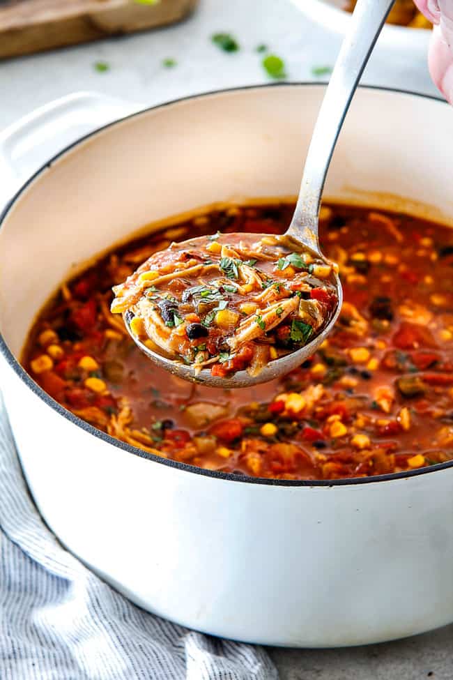 Easy 30-Minute Homemade Chicken Tortilla Soup that tastes better than any restaurant! It's accidentally healthy, easy to double/triple for a crowd, freezer friendly and tastes like it's been simmering for hours but on your table in 30 Minutes! easy Chicken Tortilla Soup in a white dutch oven with a spoonful of soup loaded with chicken, beans, corn, and tomatoes
