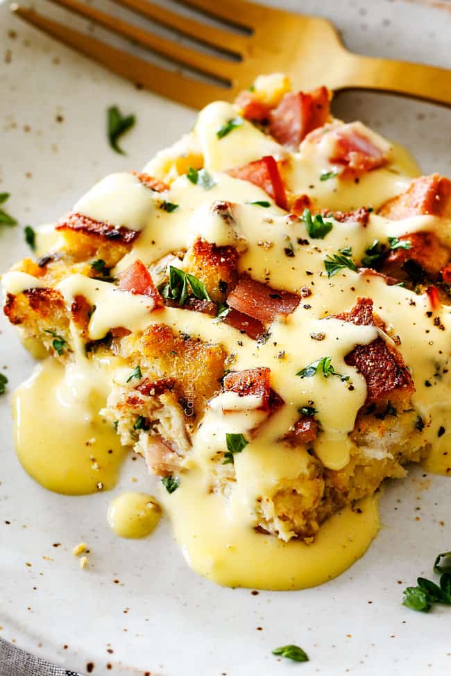 Eggs Benedict Casserole on a speckled plate being smothered by Hollandaise Sauce