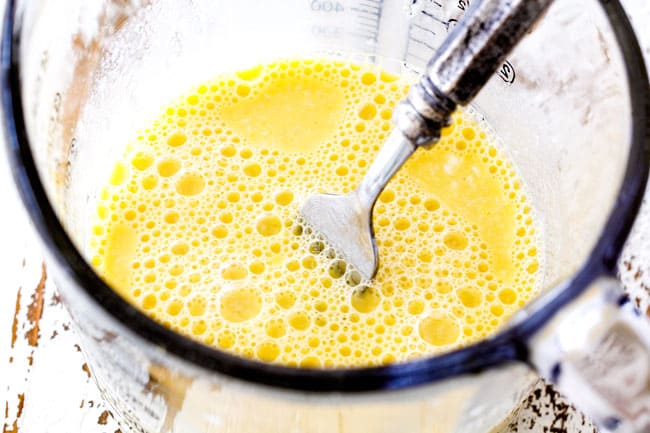 Showing how to make moist Lemon Blueberry Cake by whisking wet ingredients together of eggs, milk, lemon juice in glass measuring cup