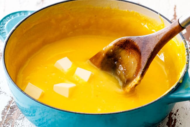 Showing how to make Lemon Curd for Lemon Blueberry Cake by melting butter in smooth lemon curd in a teal saucepan