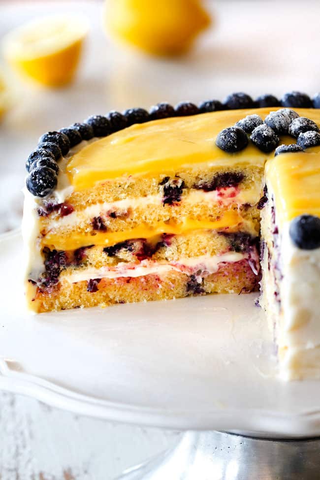 moist Lemon Blueberry Cake with Lemon Curd with a slice cut out of it showing layers of cake with lemon cream cheese frosting and lemon curd