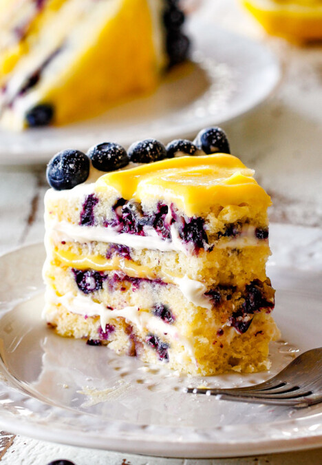 slice of lemon blueberry cake with a piece taken out of it sitting on a white plate