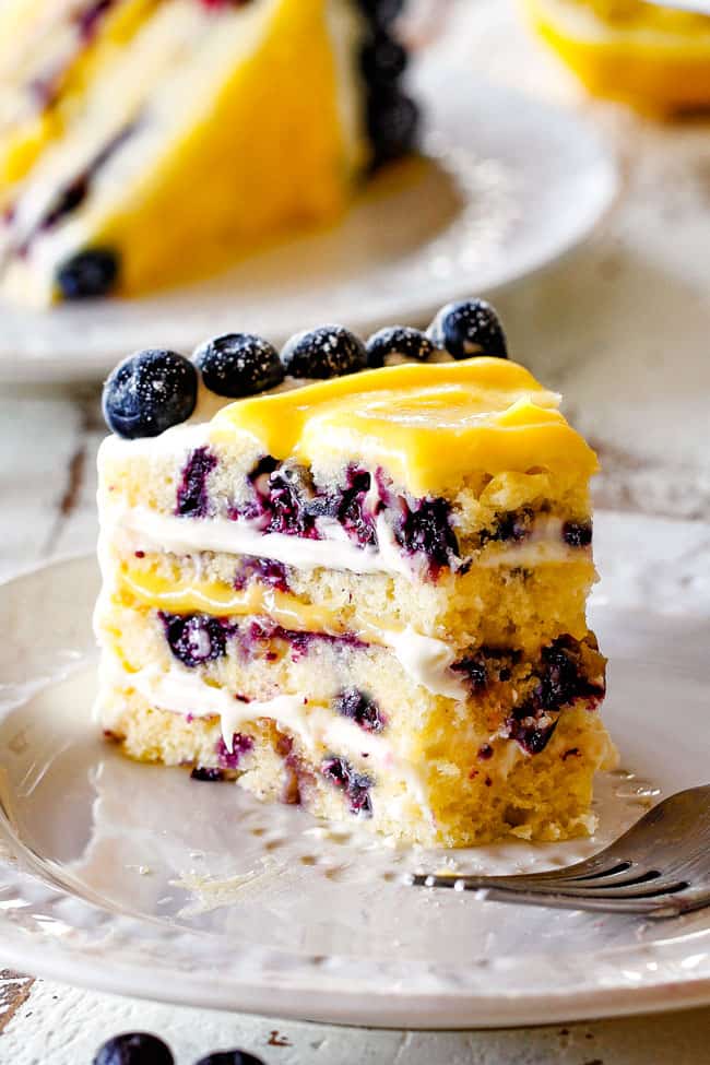 slice of lemon blueberry cake with a piece taken out of it sitting on a white plate