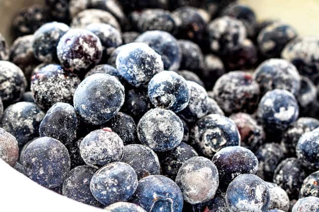 Showing how to make best Lemon Blueberry Cake by mixing blueberries with flour so they don't sink in a white bowl