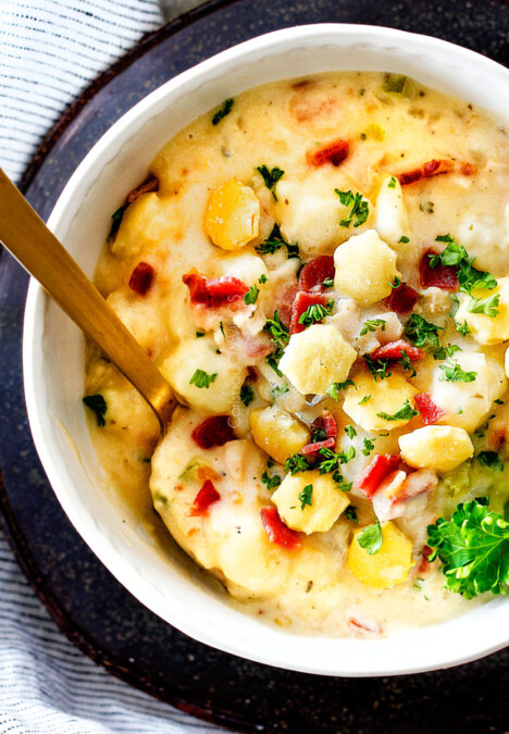 top view of white bowl England Clam Chowder with a spoon with potatoes, bacon, onions, celery and garlic
