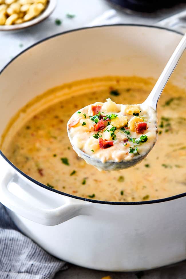 Better than any restaurant New England Clam Chowder that's SO EASY! It’s loaded with tender clams, creamy potatoes and salty, smoky bacon in a rich flavorful chowder! You can use fresh OR canned clams and both versions will blow you away! side view of the best New England Clam Chowder recipe in the world in a white Dutch oven with potatoes, bacon, onions, celery and garlic with a bowl of oyster crackers