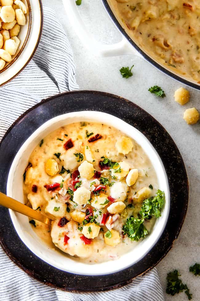 Better than any restaurant New England Clam Chowder that's SO EASY! It’s loaded with tender clams, creamy potatoes and salty, smoky bacon in a rich flavorful chowder! You can use fresh OR canned clams and both versions will blow you away! top view of white bowl of easy New England Clam Chowder recipe with a spoon garnished with oyster crackers