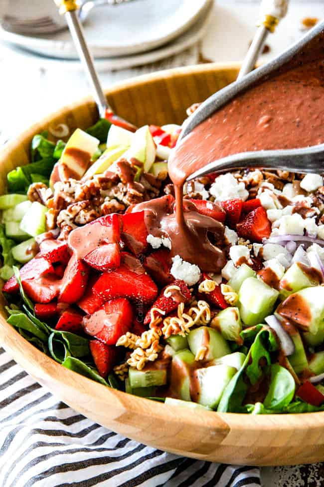 Pouring Balsamic dressing on strawberry salad in wooden bowl