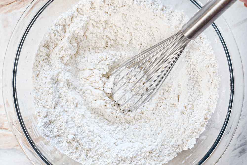 showing how to make Coconut Cake by whisking the flour, baking soda, baking powder, and salt together in a bowl