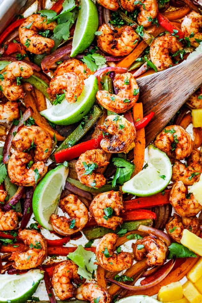 Sheet Pan Shrimp Fajitas on a baking sheet with a wooden spoon