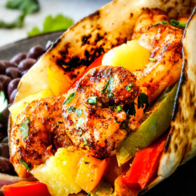 up close of oven roasted shrimp fajitas on a metal plate with bell peppers, onions and pineapple