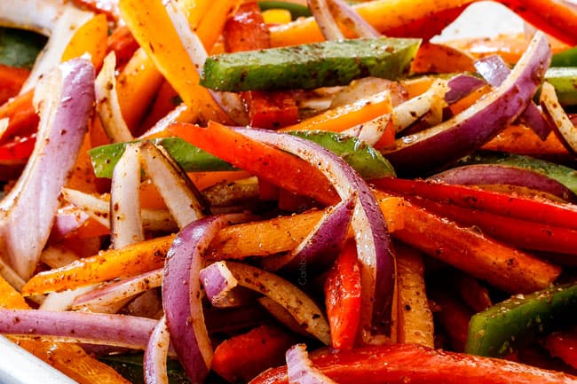 showing how to make sheet pan shrimp fajitas by mixing red bell peppers, orange bell peppers, green bell peppers and onions with olive oil and fajita seasoning on baking sheet