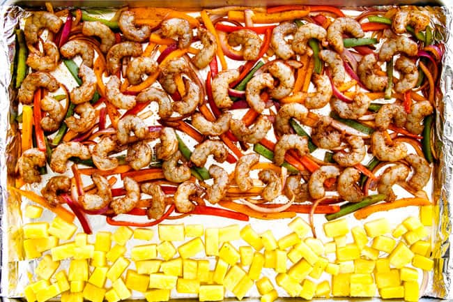 Showing how to make shrimp fajitas in oven by laying out shrimp on bell peppers and onions on a sheete pan