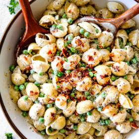 Top view of Creamy Pasta Salad with Peas and Bacon with a wood serving spoon