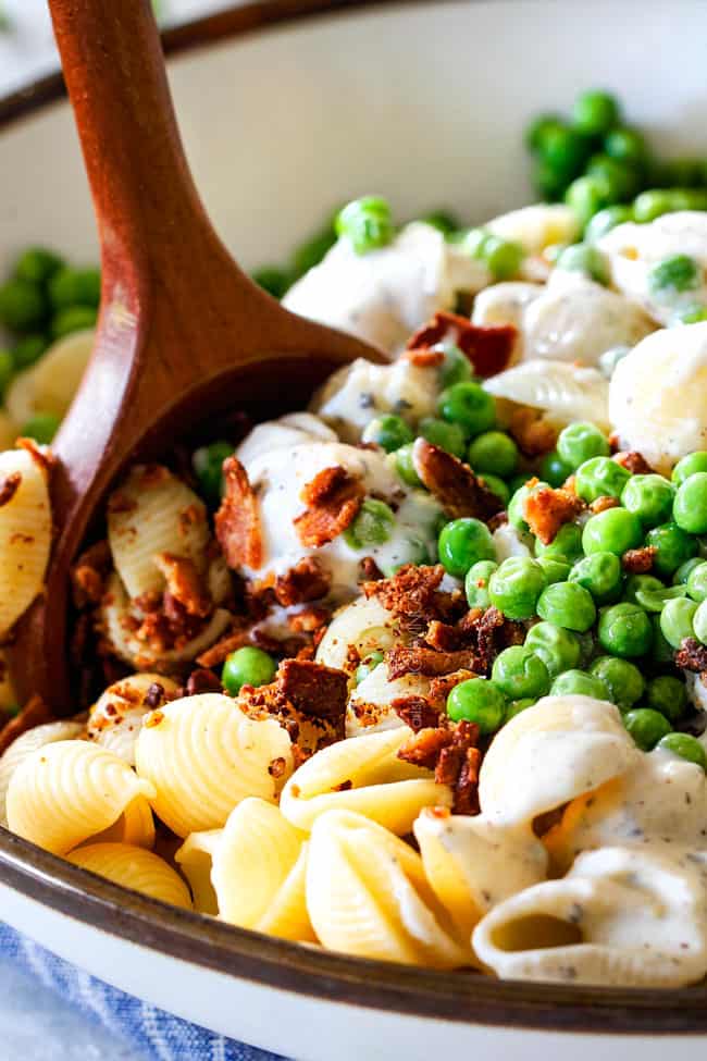 Showing how to make Creamy Pasta salad by stirring together macaroni, peas, bacon and dressing together
