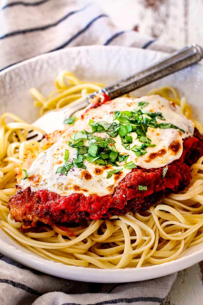 side view of a single piece of Chicken Parmesan on a bed of spaghetti on a white plate