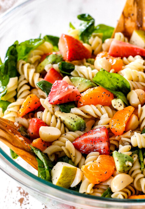 pasta, strawberries, spinach, Mandarin oranges, avocados, macadamia nuts in a glass bowl with poppy seed dressing mixed together for pasta salad
