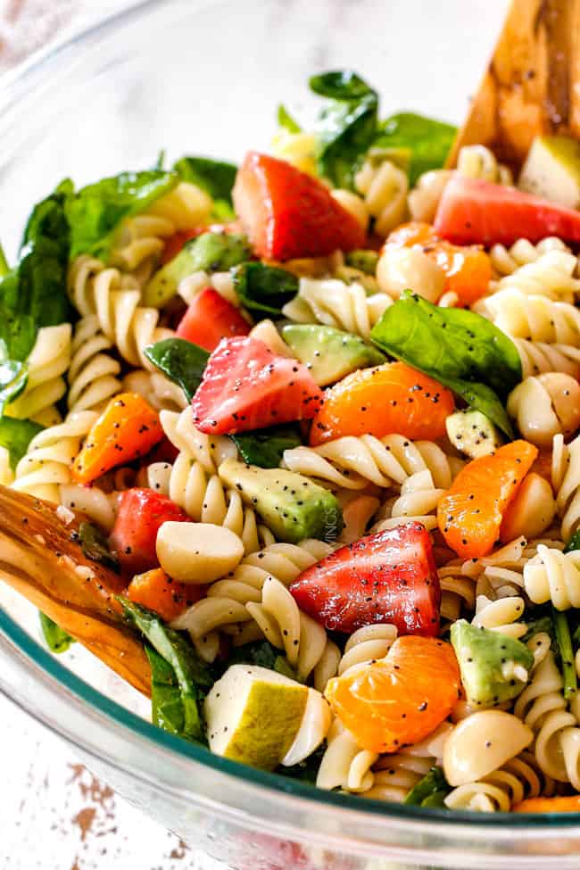 pasta, strawberries, spinach, Mandarin oranges, avocados, macadamia nuts in a glass bowl with poppy seed dressing mixed together for pasta salad