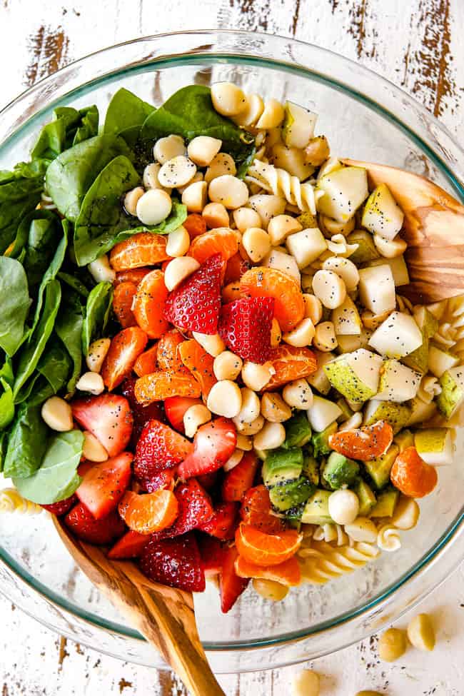 Mixing pasta, strawberries, spinach, Mandarin oranges, avocados, macadamia nuts and past in a glass bowl for pasta salad