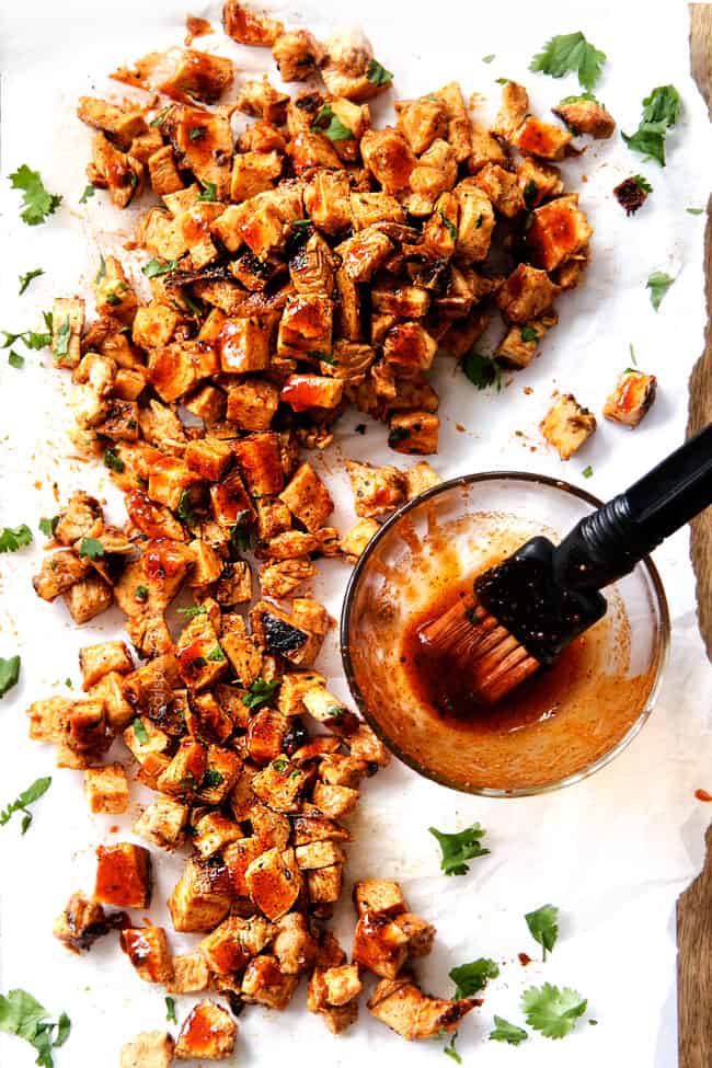 chopped Buffalo chicken on a cutting board with Buffalo Sauce in a glass bowl
