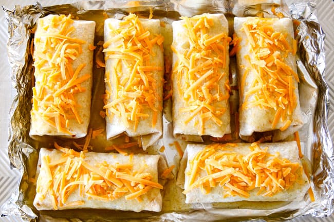 showing how to make wet burritos by adding cheese and enchilada sauce to burritos on a baking sheet