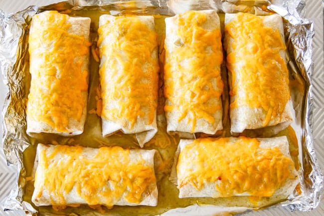 green enchilada sauce smothering wet burritos with melted cheese coming out of the oven