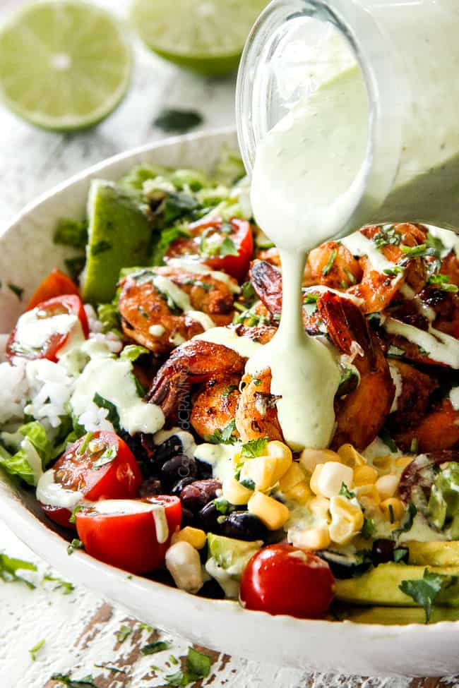pouring creamy Cilantro Lime Dressing over a bowl of shrimp, corn, tomatoes and black beans