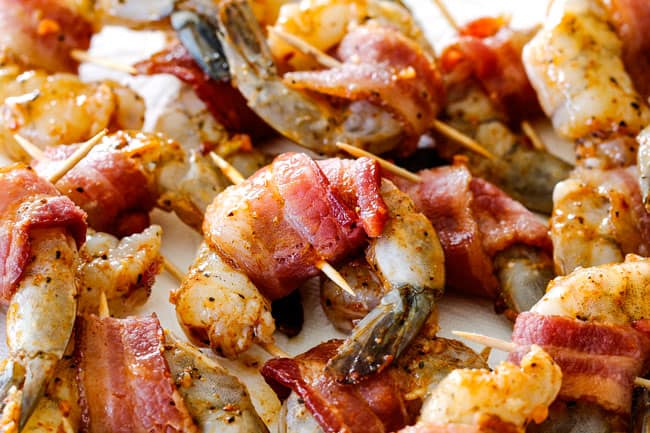 showing how to make bacon wrapped shrimp by wrapping bacon around raw shrimp and securing with toothpick