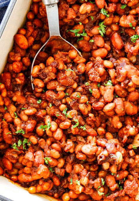 top view of homemade Baked Beans in a blue 9x13 baking dish with green parsley