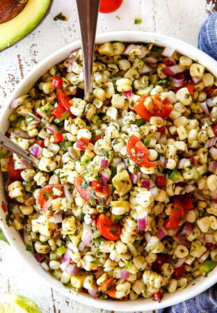 Fresh Corn Salad mixed together in a white bowl with silver spoons