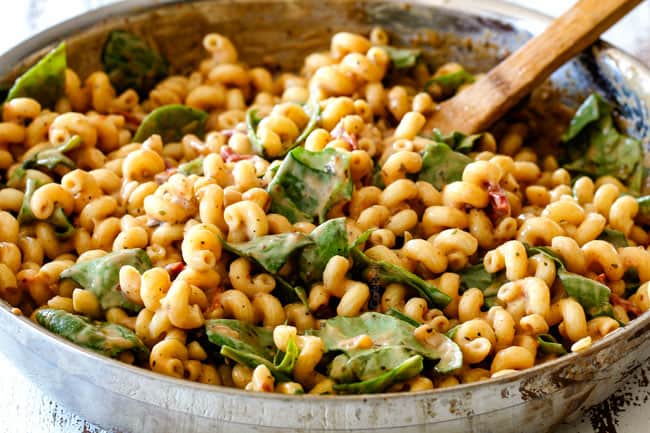 showing how to make Sun-Dried Tomato Pasta by stirring sauce and spinach into pasta