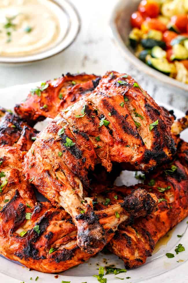 Side view of authentic Tandoori Chicken Recipe with marinated and slashed chicken on a white platter with yogurt dip
