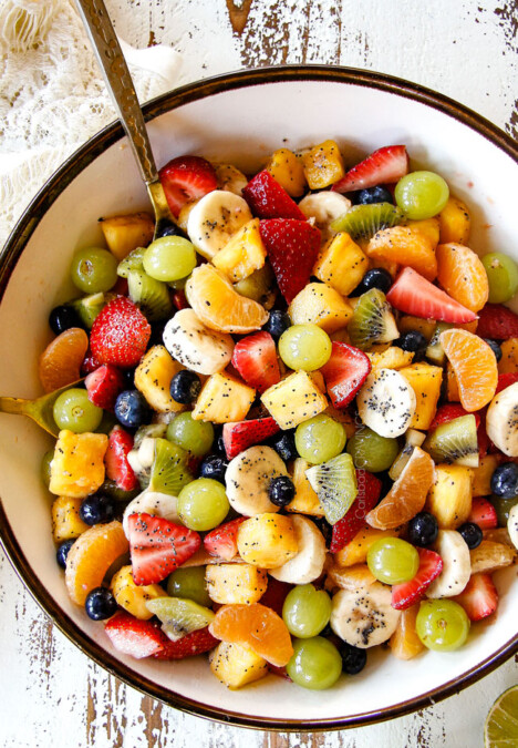 top view of best fruit salad in bowl with pineapple, strawberries, blueberries, bananas, kiwis, grapes and oranges