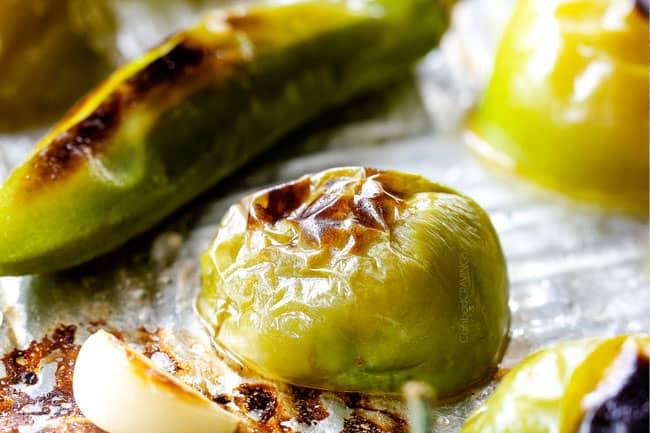 up close of charred tomatillos and serrano peppers on a baking sheet showing how to make homemade salsa verde