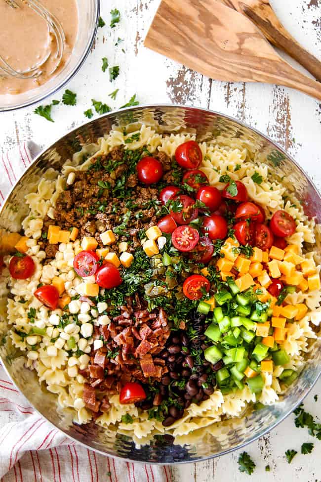 showing how to make Cowboy Pasta Salad by adding ground beef, black beans, corn, tomatoes, jalapenos, cilantro and barbecue sauce,