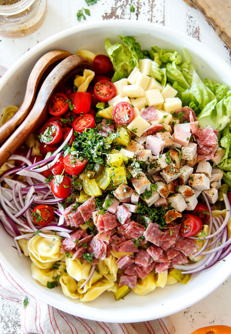top view of Cuban pasta salad with cheesy tortellini, cubed pork roast, ham, salami, Swiss cheese, tomatoes, pickles pickled jalapenos, red onions, Romaine lettuce and cilantro
