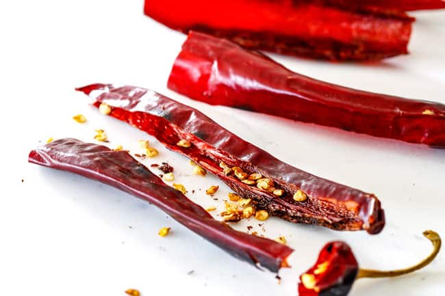 showing how to make al pastor marinade by removing seeds from guajillo chiles on a white cutting board