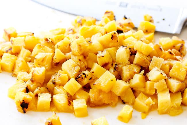 showing how to make authentic Tacos Al Pastor by chopping grilled pineapple on a white cutting board
