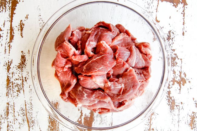 showing how to make tacos al pastor with thinly sliced pork in a glass bowl