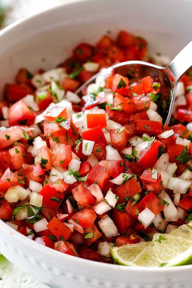 sidea spoonful of easy pico de gallo with a spoon in a white bowl