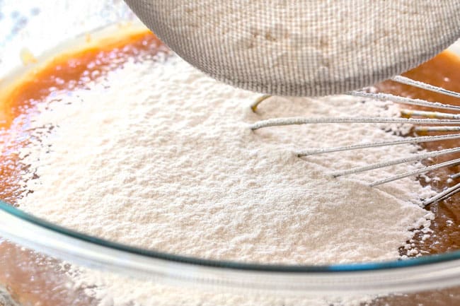 showing how to make pumpkin bars by sifting together the flour and dry ingredients in a glass bowl