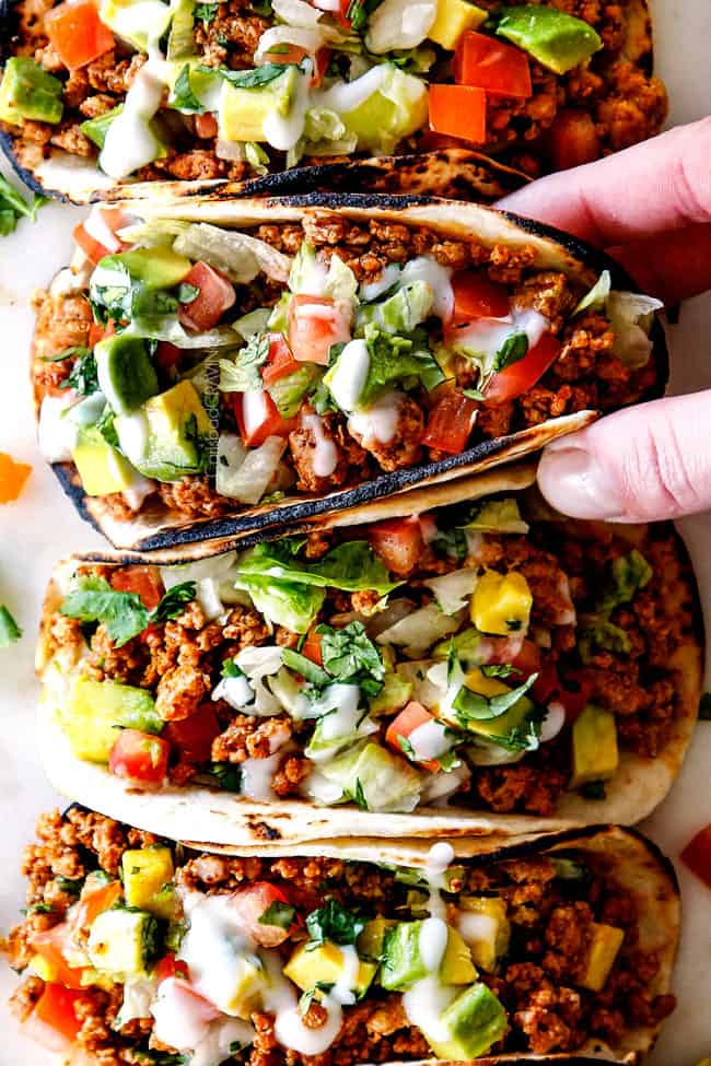 up close top view of a row of easy turkey taco with ground turkey, taco seasoning, lettuce, sour cream, tomatoes and avocados